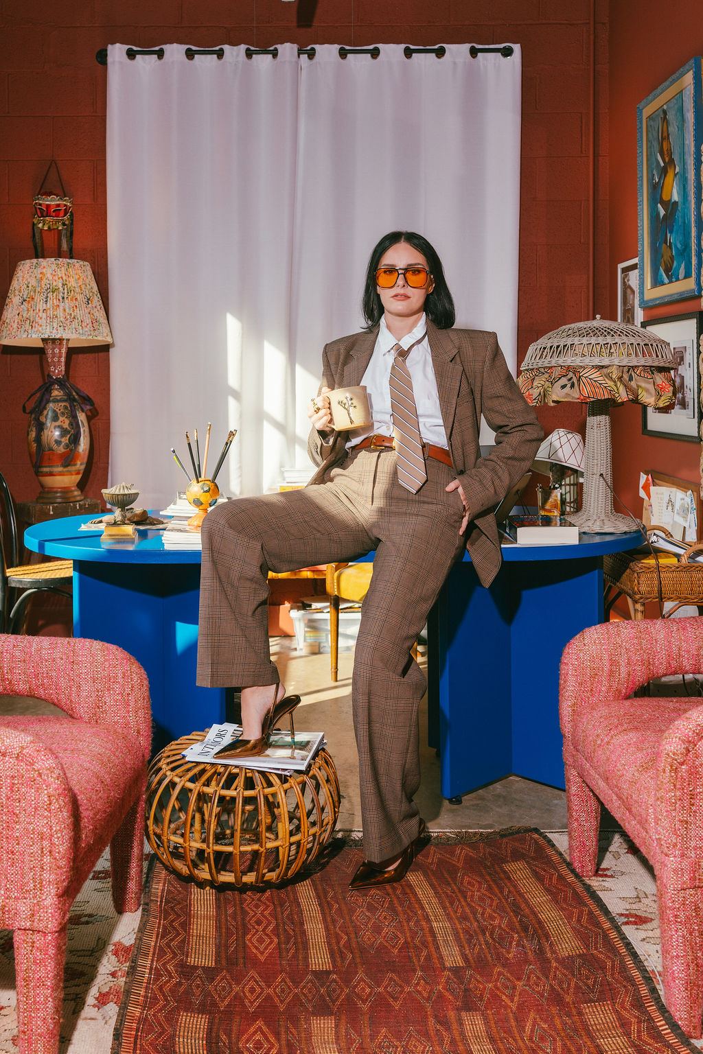 Jac Bollenbacher, founder of Hestia Studio, in a plaid suit holding a mug in her studio