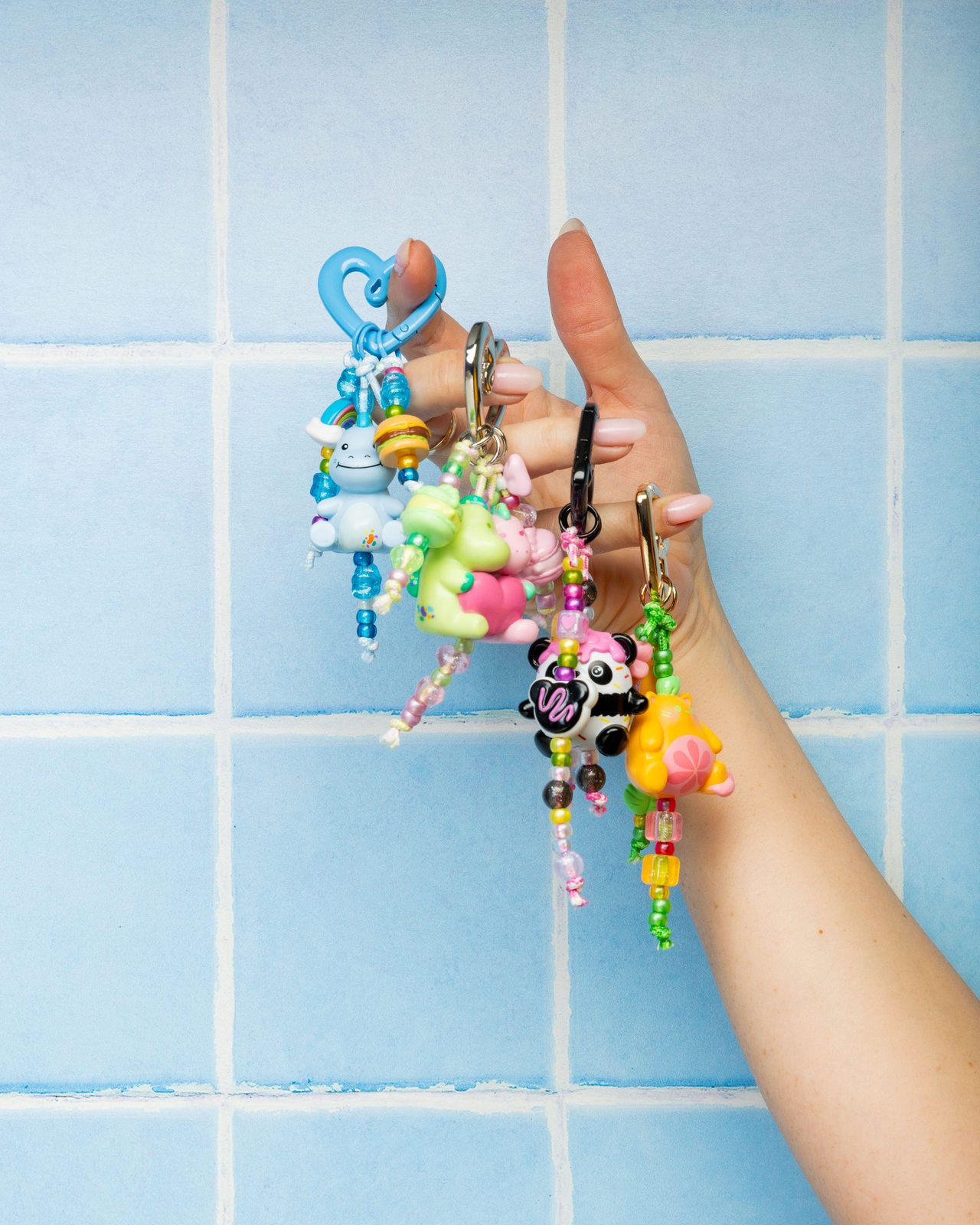 Hand holding beaded character keychains against a pale blue tiled wall