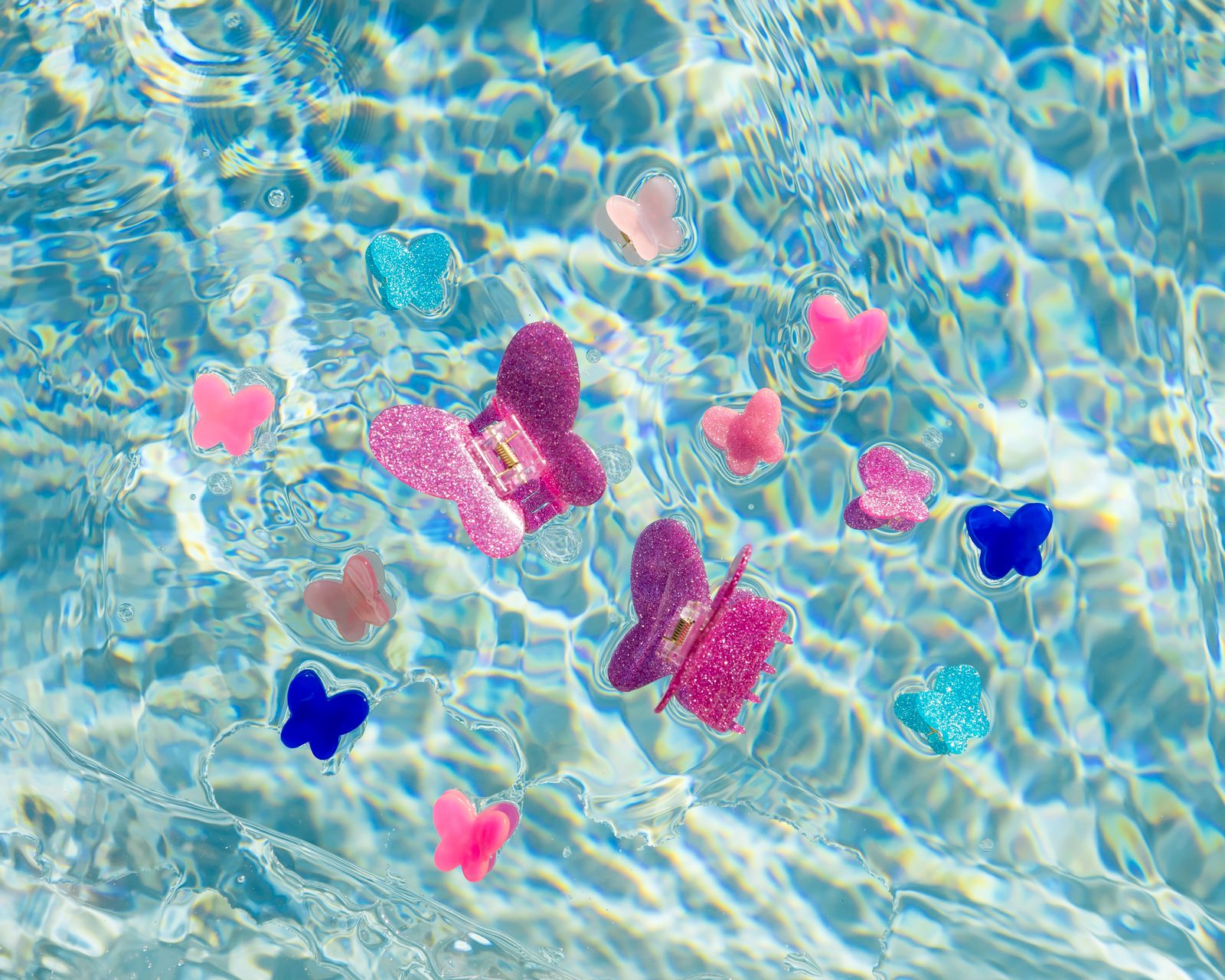 Glittery pink, purple, and blue butterfly claw clips floating in a sparkling pool
